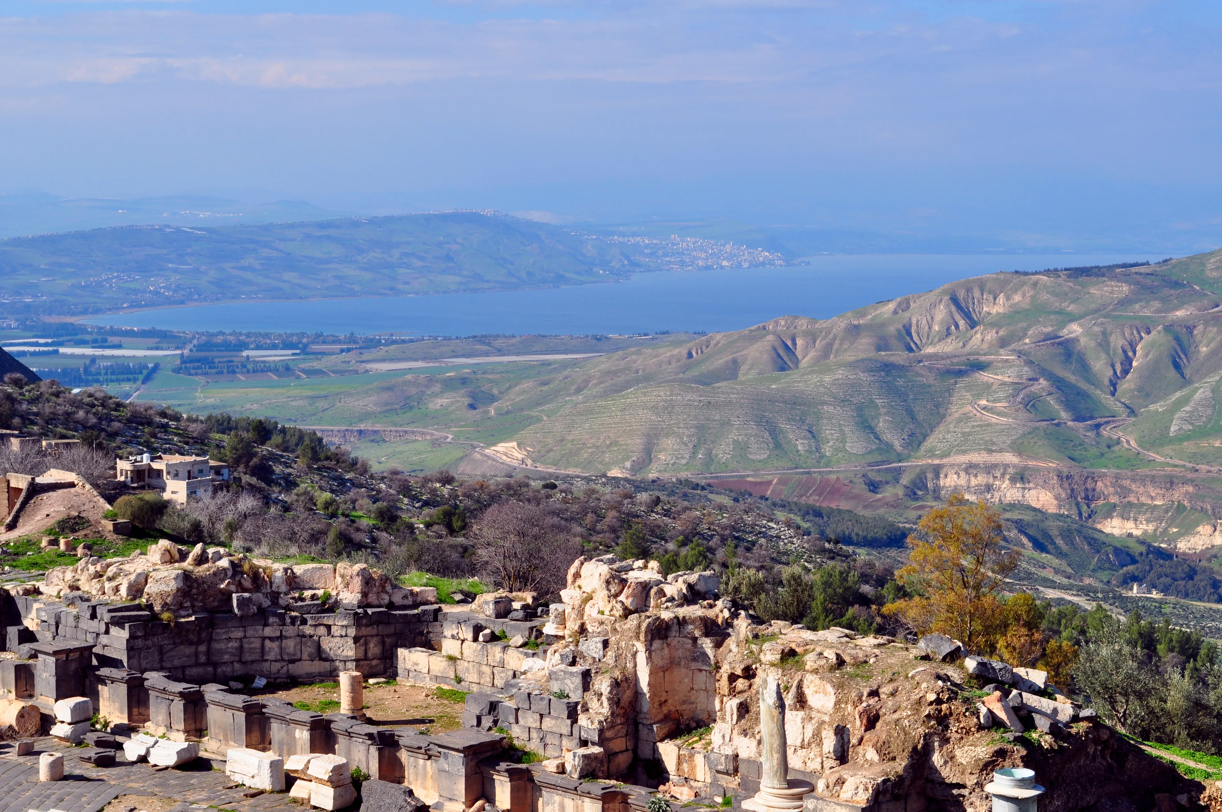 Ancient stone ruins at Umm Qais overlooking green hills and a large blue lake in the distance.