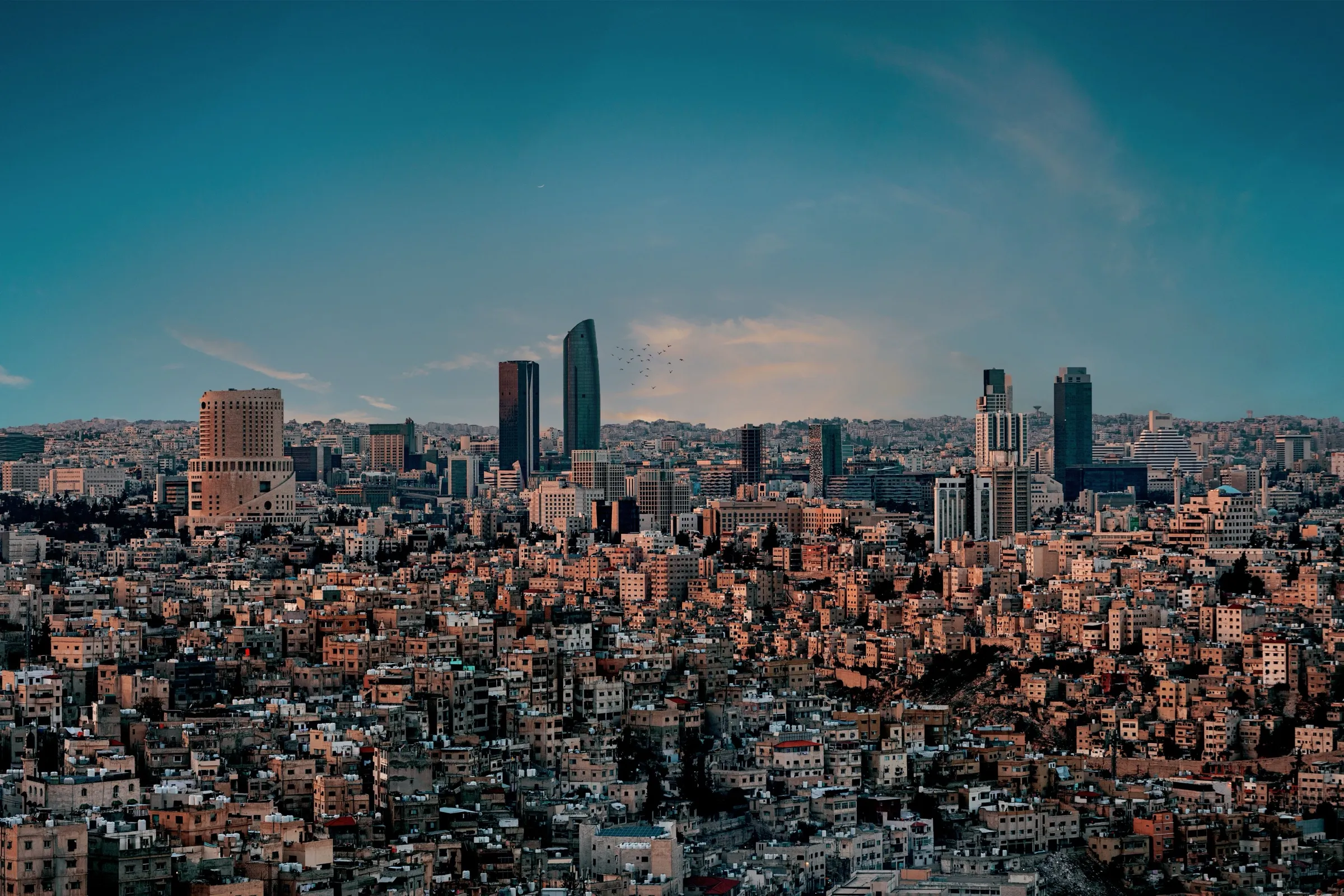 Amman at dusk, the Abdali towers rising out of dense stone housing that runs to the horizon.