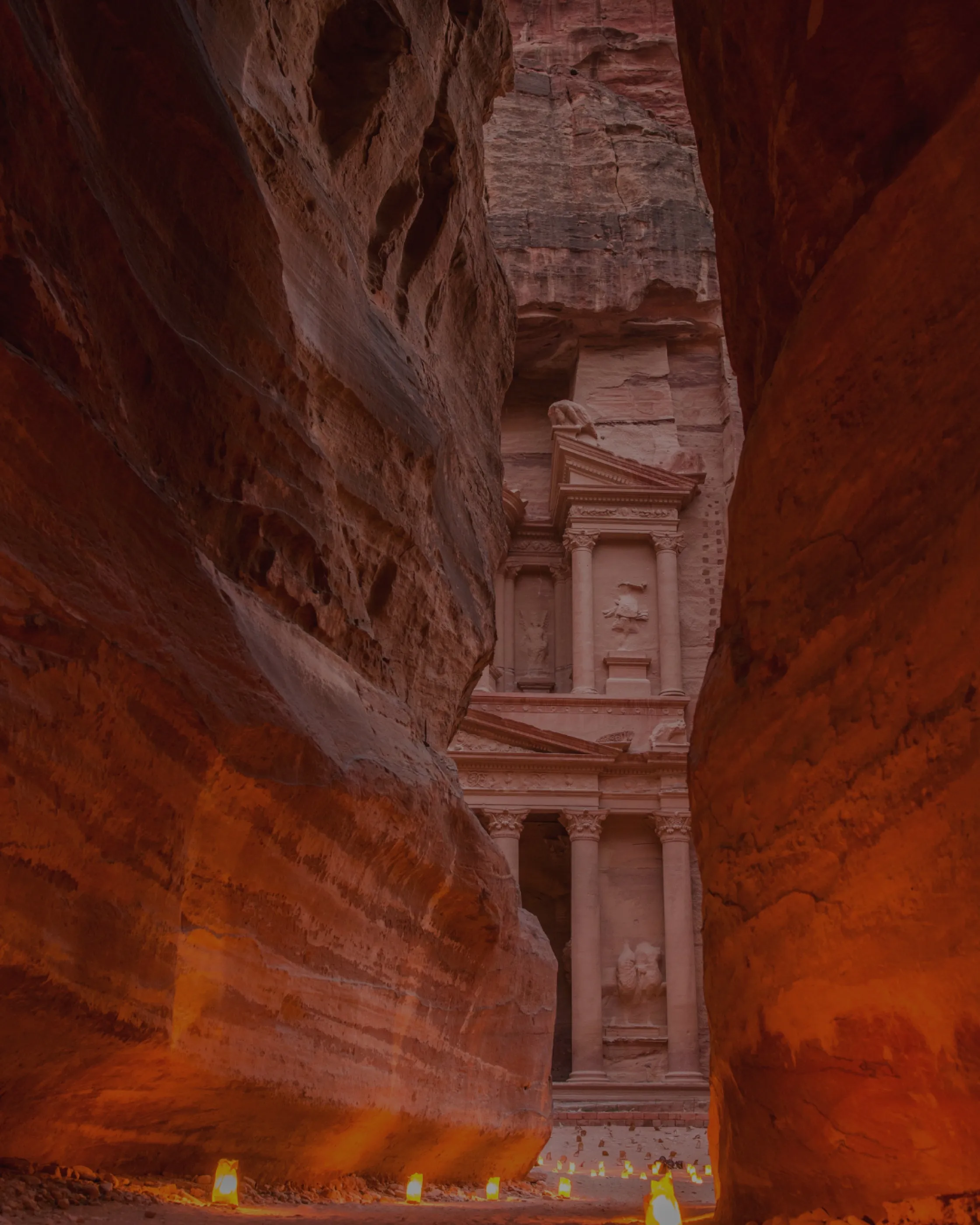 The Treasury at Petra seen through the narrow gap of the Siq, lit by candles set along the path.
